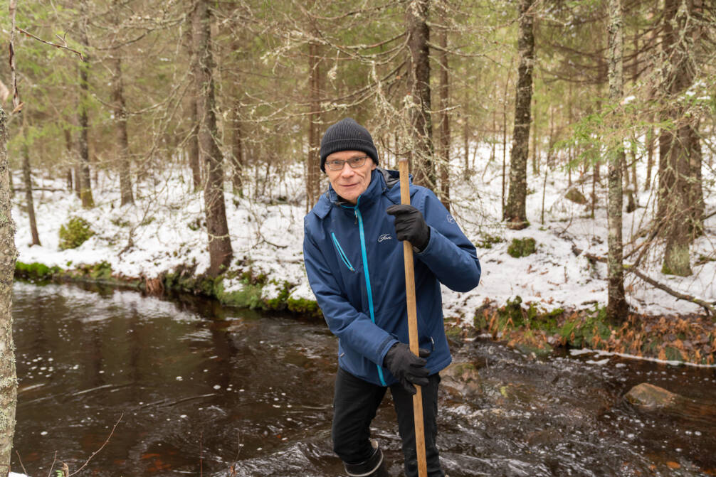 Professori Timo Muotka seisoo metsäpurossa maastossa saappaat jalassa.