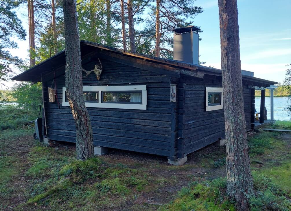 mustahirsinen mökki mäntymetsässä järven rannalla